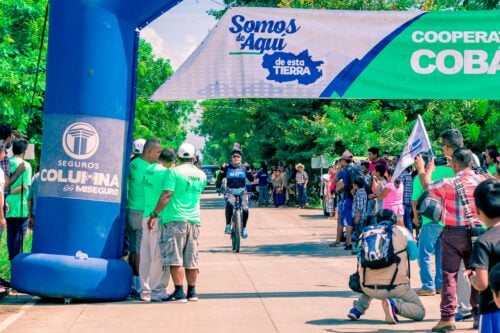 A cyclist reaches the finish line, cheered by a vibrant crowd at an outdoor race event.